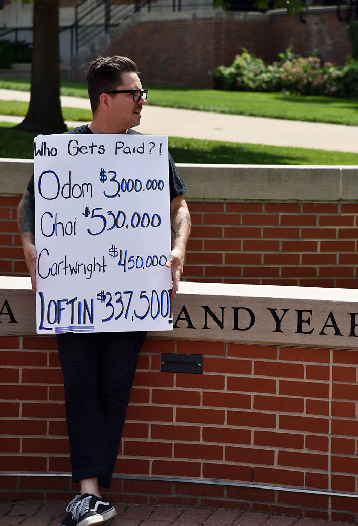 Shane Johnson holds a sign showing the salaries of MU leaders during a rally